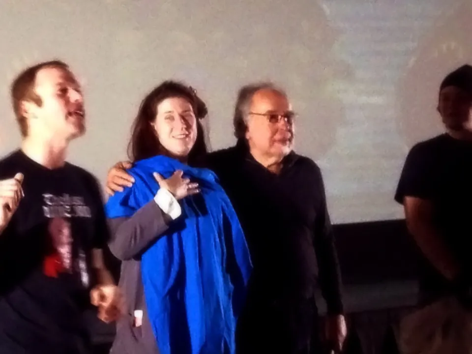 Mary Poplin on stage with Peter Beagle and two other people in front of a projection screen, with a blue T-shirt in the foreground